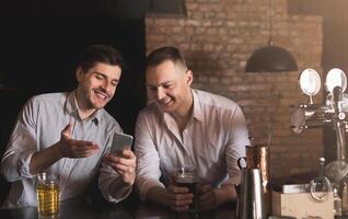 Two happy friends enjoying fresh beer at pub and browsing social networks on mobile. Technologies, online communication and internet addiction, copy space photo