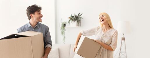 Young Couple Laughing Carrying Packed Boxes With Things Entering New Place. Moving Apartment Concept. Selective Focus photo