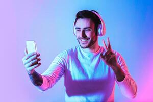 Communication online. Smiling guy showing peace sign in smartphone photo