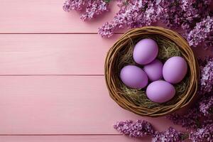 A wicker basket filled with purple eggs surrounded by blooming lilacs on a soft pink table photo