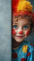 A young child with curly hair smiles playfully while dressed as a clown near a wall photo