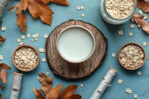 Oat milk served in a ceramic cup on a wooden surface surrounded by oats and green leaves photo