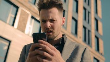 Angry mad caucasian businessman business man using phone reading bad news on internet outdoors near office building furious stressed male entrepreneur annoyed with online problem mobile system failure photo