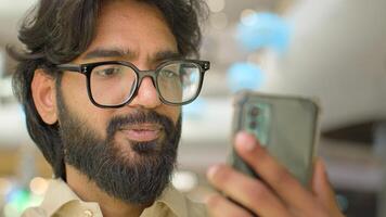30s Indian bearded guy talk call conversation on smart phone. Modern wireless technology usage. Arabian man in eyeglasses businessman talking to mobile web camera remote communication conference photo