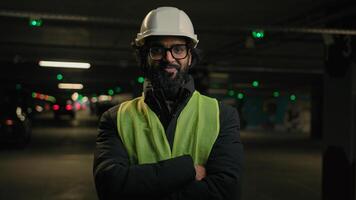 Indian man handyman worker contractor hands crossed posing in parking smiling mechanic in helmet, glasses power pose at factory warehouse manufacture. Arabian male builder engineer fitter in hard hat photo
