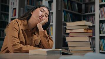 Tired sleepy asian woman student fall asleep in university library exhausted drowsy girl sleeping on desk with stack books feel fatigue doze sleep on table break from studying exam preparation concept photo