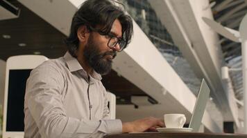 Pensive Indian businessman typing on laptop remote working internet concentrated arabian man manager analyzing digital data create business plan using computer app indoors send email in social network photo