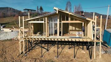 Wooden house under construction on a hillside - A partially built wooden house with exposed framework on a hillside, featuring modern construction techniques and materials under a clear blue sky. video