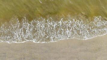Overhead View of Gentle Waves on Sandy Beach. Aerial perspective of small waves creating intricate patterns of foam as they wash over a sandy shoreline, evoking serenity. video