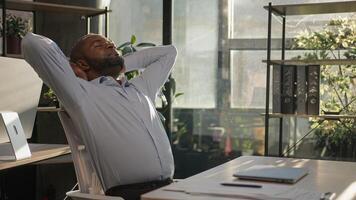 Relaxed African American mature businessman senior happy man finish computer work close laptop relaxing in sunny warm comfortable office male specialist stretch muscles put hands behind head day end photo