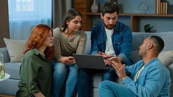 Multiracial friends working online with laptop order delivery at home diverse group men and women colleagues using computer web app in living room creative team talk discuss ideas startup brainstorm photo