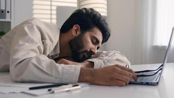 Lazy weary sleepy male manager tired exhausted Arabian Indian businessman employee working computer boring remote job man fall sleep on desktop napping in office overwork fatigue no energy sleeping photo