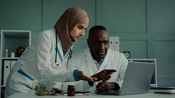 Multiracial doctors colleagues discuss teamwork african man and arabian woman two professional medical workers talk about healthcare check MRI scan use computer app doing online research X-ray results photo