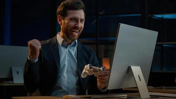 Adult businessman employee working in evening office happy male gamer Caucasian man take break playing console game on computer with gaming controller using joystick gamepad play virtual match photo