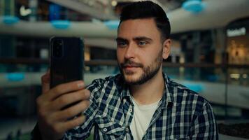 Smiling arabian caucasian male blogger businessman look at mobile phone camera talk call in shopping mall happy young man chatting online recording blog use modern tech for remote communication photo