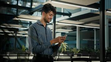 Smiling happy millennial arabian businessman ethnic man professional office worker male guy use smartphone browsing mobile apps look at cellphone texting message chatting online make order in internet photo