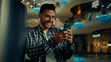 Young man blogger arabian hispanic businessman stand in shopping center look at mobile screen texting message email read positive news on cellphone buying goods online use wireless internet connection photo