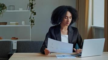 African teacher worker business woman work with graphics documents at home office check documentation enter financial data to laptop processing online information paying bills in computer banking app photo