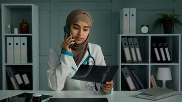 Young doctor arabian turkish woman in hijab islam religion female radiologist work in surgical medicine talking mobile phone examine x-ray broken bones image share with patient bad tomography result photo