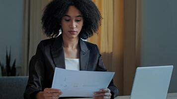 African teacher worker business woman work with graphics documents at home office check documentation enter financial data to laptop processing online information paying bills in computer banking app photo