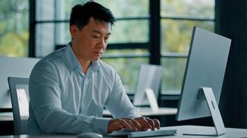 Portrait concentrated male office worker web-designer asian middle-aged man businessman sit at workplace use desktop computer developing tech program analyze online trading market finance digital data photo
