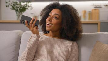 Happy African American woman on couch ethnic smiling female girl mobile phone send audio message using cell speakerphone convenient usage smartphone record voice mail recording chat voicemail at home photo