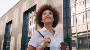 Stylish happy African American businesswoman holding coffee cup take away drink attractive girl in city business woman beautiful lady walking outdoors joyful female walk on street near urban building photo