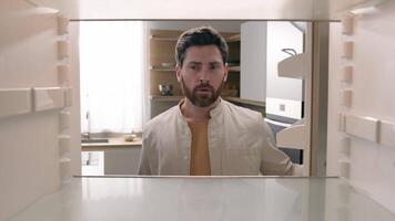 Hungry Caucasian bachelor man looking for food in empty fridge finding no meal products feeling sad disappointed poor unemployment need delivery service POV point of view from inside refrigerator photo