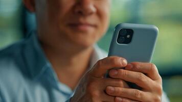 Unknown asian man businessman worker modern user senior entrepreneur hold in hands phone search online information use mobile business apps wifi 5g connection in office texting messages on smartphone photo