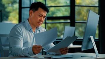 Disappointed angry Asian office manager mature man specialist lawyer banker work with paper documentation read legal documents check error bankruptcy problem negative incorrect result business failure photo