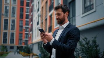 Handsome successful businessman caucasian man stand near modern residential building in city working outdoor use phone digital mobile app on way search information online texting messages distant chat photo