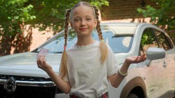 Funny confused adorable Caucasian little girl child kid smiling unsure schoolgirl looking camera showing driving license car rental service automobile what shrugging shoulders gesture puzzled at city photo