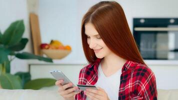 Satisfied caucasian female shopper customer enters number of bank credit card for financial transaction in mobile phone app makes donate pays internet order shopping online purchases booking e-tickets photo