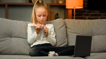 Concentrated pupil girl making homework at copybook on cosy sofa writing math tasks of elementary school subjects practicing calligraphic handwriting learn language by online educational lesson photo