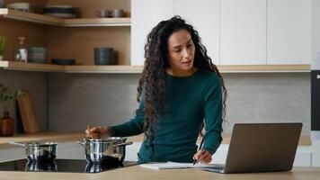 Arabian woman mother cooking lunch meal healthy food in modern kitchen writing internet recipe using helpful cookery website on laptop cookbook menu app watching online tutorial culinary at home photo