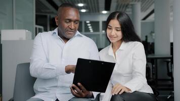 Diverse business partners sit in office discuss paper instruction african businessman show documentation in folder tablet to arabian female colleague explain insurance contract benefits negotiating photo