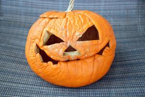 Wrinkled carved pumpkin with a spooky expression on a fabric background. photo