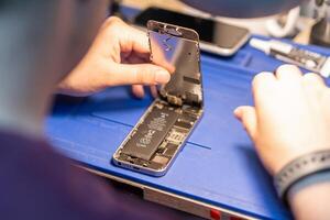 A technician is meticulously replacing the battery of a smartphone in a well-organized repair workshop filled with tools photo