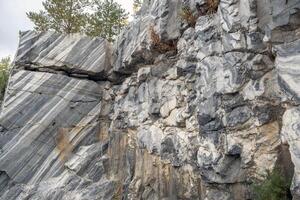 A detailed exploration of a marble quarry reveals vibrant patterns in stone, surrounded by greenery and a dynamic sky above photo