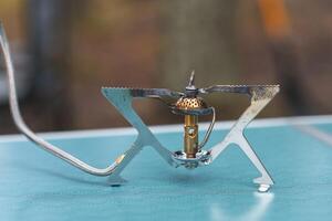 A portable camping stove is assembled and awaiting use on a bright blue table in a tranquil outdoor setting photo
