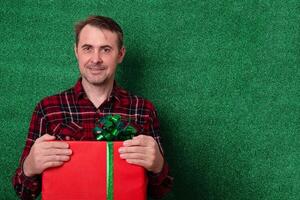 a man with a gift in his hands on a green background looks into the frame. holidays new year, valentine's day photo