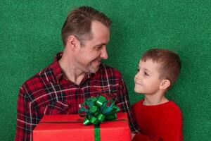 a man with a small son are holding a large gift in cookies on a green background and looking at each other. family congratulations. holidays new year, valentine's day photo