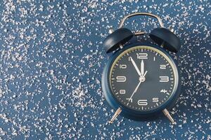 Alarm clock over a cold blue background with scattered snow photo