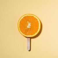 Summer concept orange on a stick instead of ice cream - Piece of juicy orange on yellow background and bright sunlight - Minimal creative concept photo