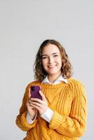 Young Business Woman Using Smartphone at White Background. A portrait of a smiling young businesswoman holding a smartphone, engaged in browsing apps, checking online content, and texting messages. photo