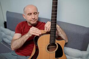 man putting a strap on a guitar, close-up at home. Relaxing and sitting on sofa photo