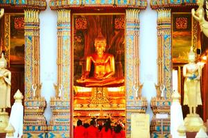Golden Buddha Statue in Ornate Temple with Intricate Details and Devotees in Vibrant Red Attire photo