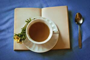 Cup of tea on an open book with flowers on a blue tablecloth photo