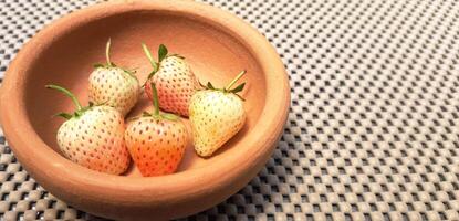 Blurred image of white strawberries in a clay bowl. photo