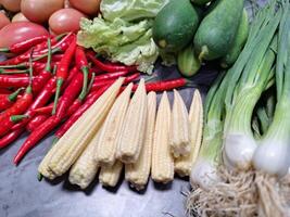 Photo of a pile of vegetables on a table, tomatoes,chili, cucumber, lettuce, spring onion, corn.